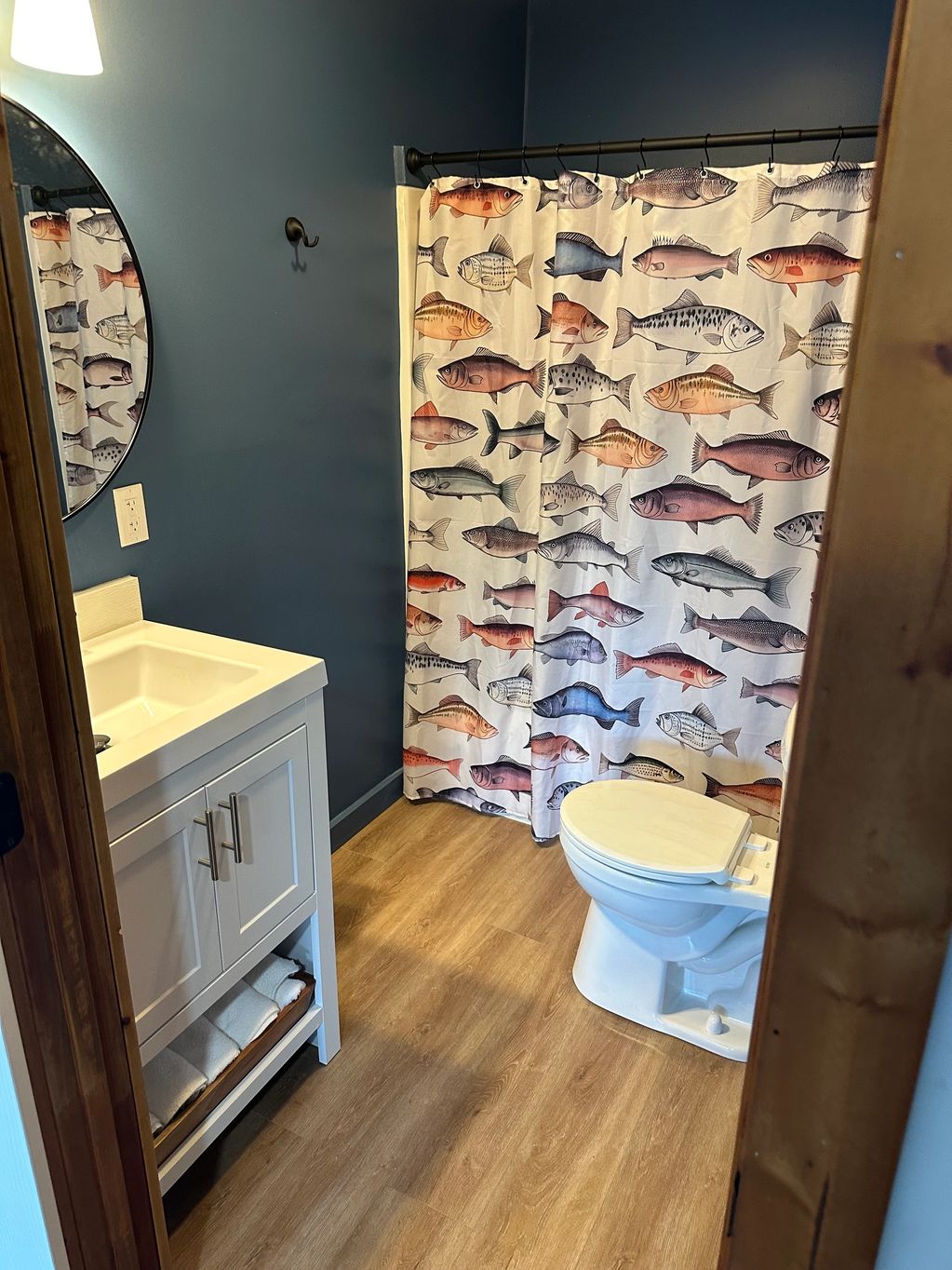 Bathroom with fish-themed shower curtain and wooden floor.