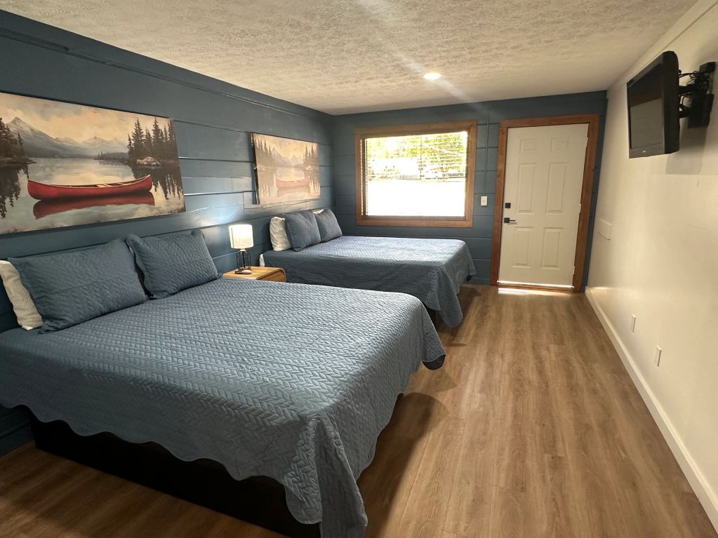 Cozy bedroom with two blue beds, wooden floors, and nature-themed wall art.
