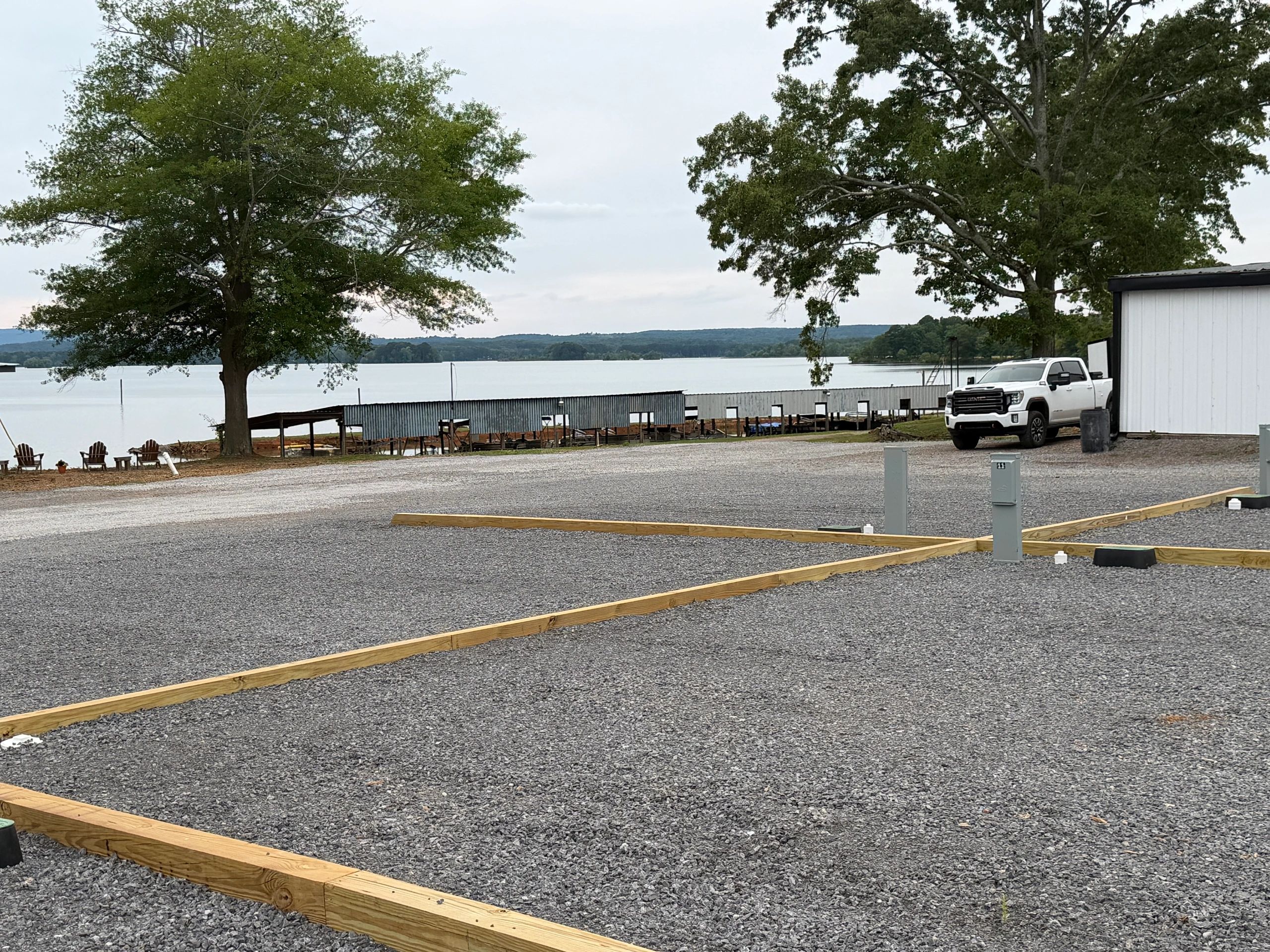 Gravel lot with wooden borders, trees, a white truck, and a lake in the background.