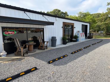 Small white building with outdoor chairs and parking stops on a gravel lot.