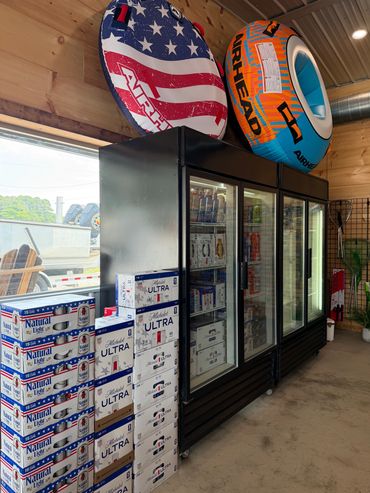 Stacked beer boxes next to refrigerated display coolers in a wooden interior store.