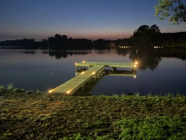 A serene dock illuminated by soft lights on a calm lake at dusk.