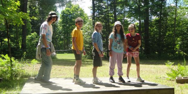 Five kids standing on a wooden platform in a forest.
