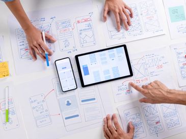 Team collaborating on mobile app design and wireframes with digital devices and sketches.
