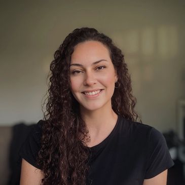 Smiling woman with curly hair wearing a black shirt against a neutral background.