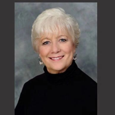 Smiling elderly woman with short white hair and black turtleneck.