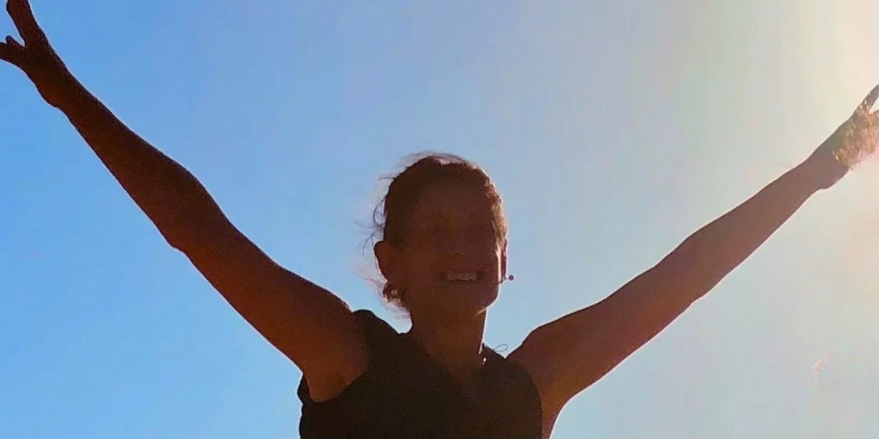 Deborah Annes with her arms spread wide and backlit by the sun.