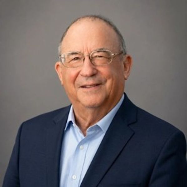 Smiling elderly man in glasses and suit jacket.