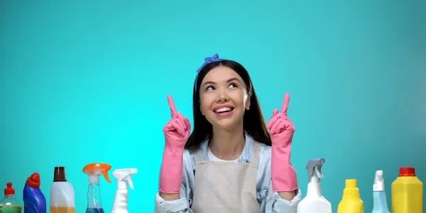 Woman with cleaning gloves pointing upward surrounded by cleaning supplies.