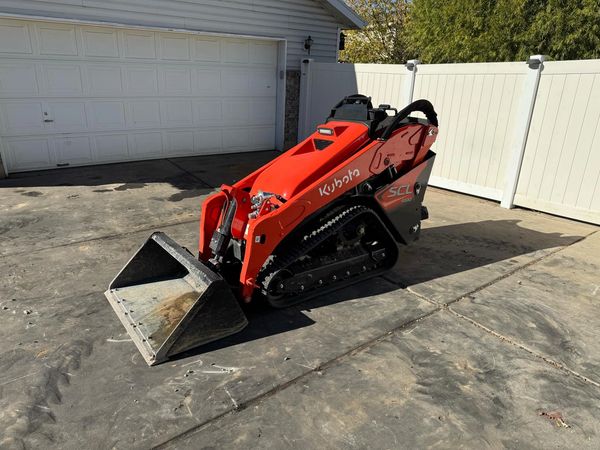 Kubota SCL 1000 Mini Skid Steer with 40 inch bucket in front of garage and white vinyl fence
