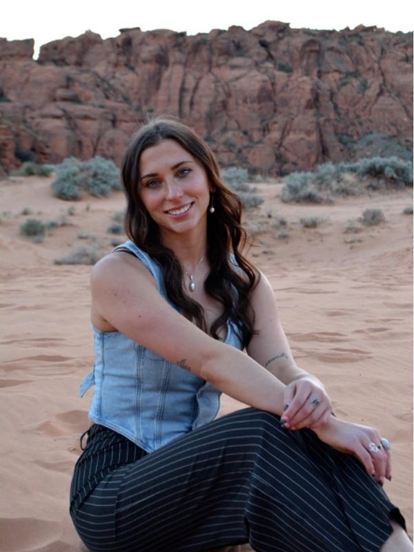 Woman sitting on sandy desert terrain, smiling.