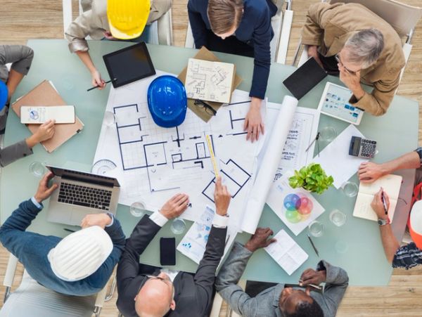 Group of architects and engineers collaborating over blueprints and laptops.