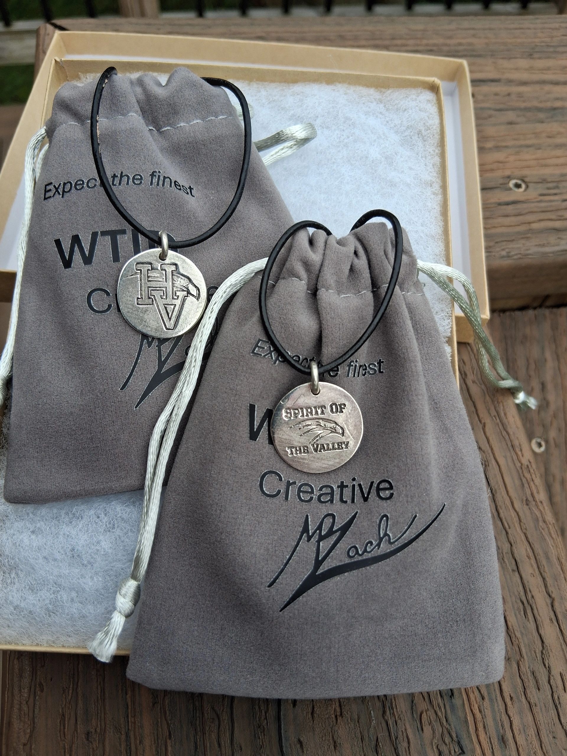 Two necklaces with round pendants on gray drawstring bags.