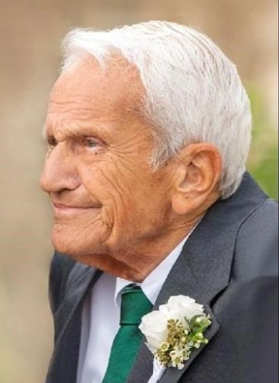Elderly man with white hair wearing a suit and boutonniere.