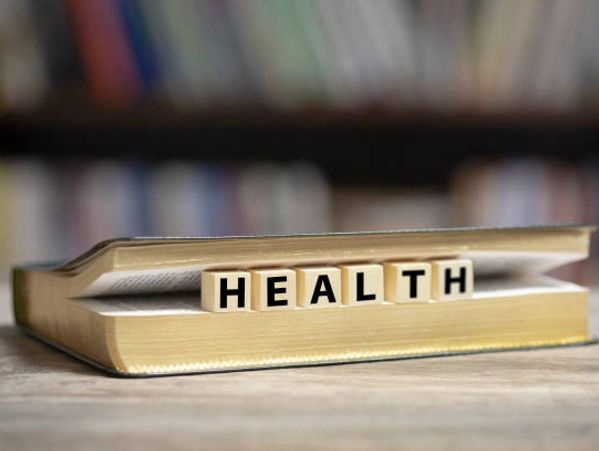 Wooden blocks spelling HEALTH inside an open book on a wooden surface.