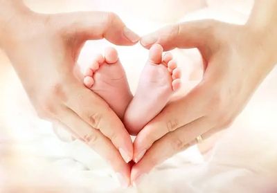 Hands forming a heart around baby feet.