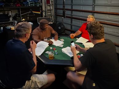 Four men playing poker with cards and chips in a garage setting.