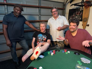 Four men posing around a poker table with chips and cards.