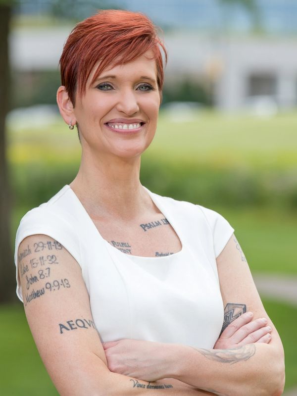 Smiling woman with red hair and multiple tattoos on her arms and chest.