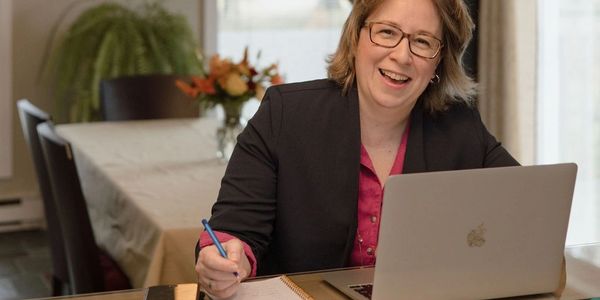 Smiling woman working on a laptop and writing notes at a table.