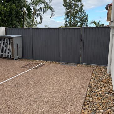 Gray metal gate and fence with a gravel driveway and landscaping stones.