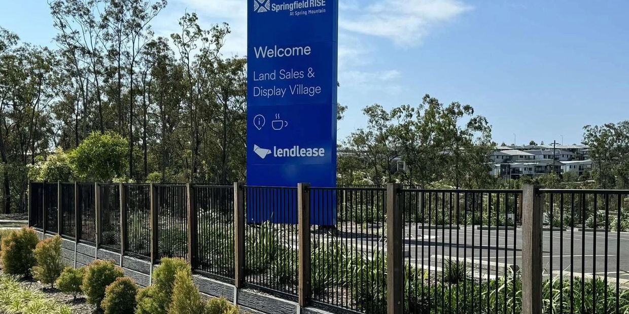 Black metal fence along a landscaped roadside with a blue land sales sign.