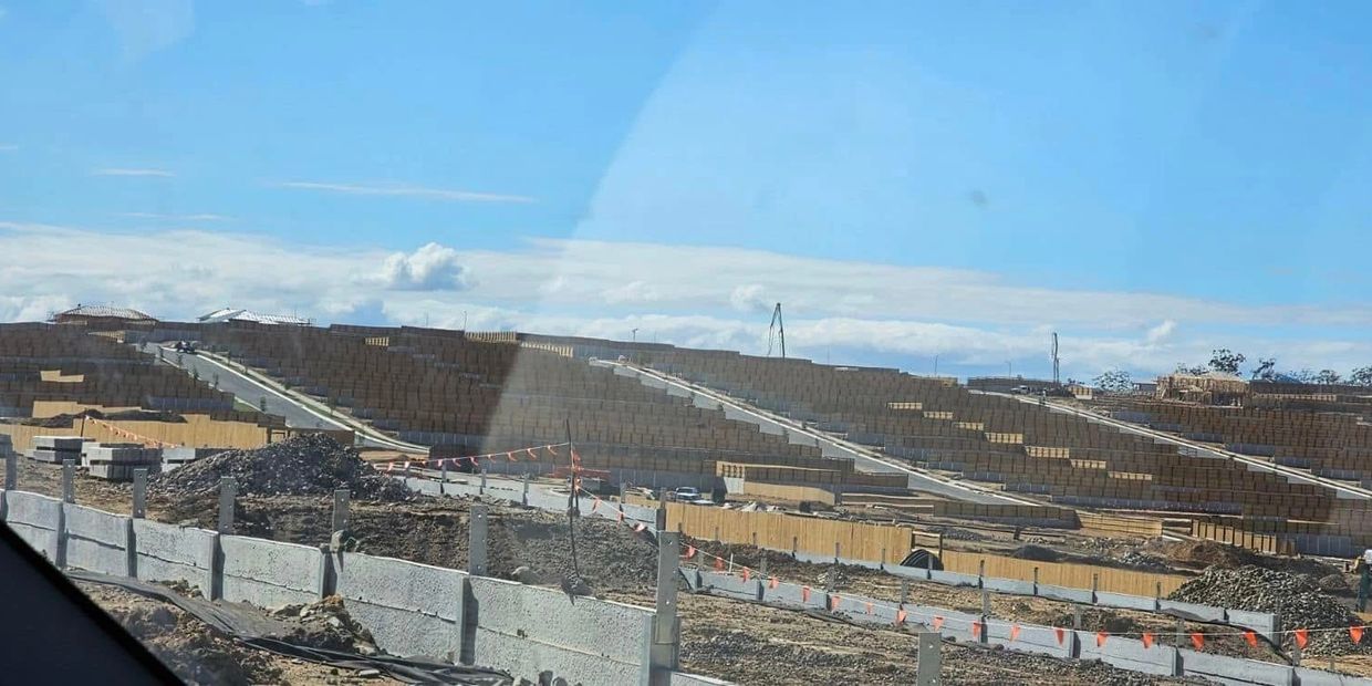 Construction site with stacked wooden pallets and concrete barriers under a clear blue sky.