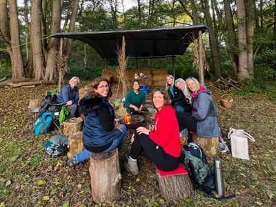Women by a woodland shelter enjoying therapeutic outdoor activities during a bushcraft workshop