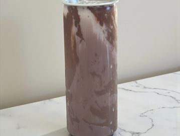 A chilled can with chocolate and milk swirls on a marble surface.