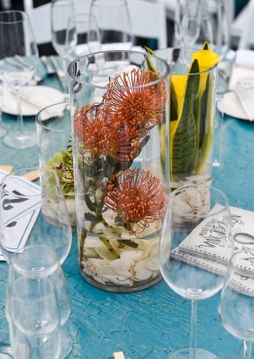 Elegant floral centerpieces in glass vases on a blue tablecloth at a formal dining setting.