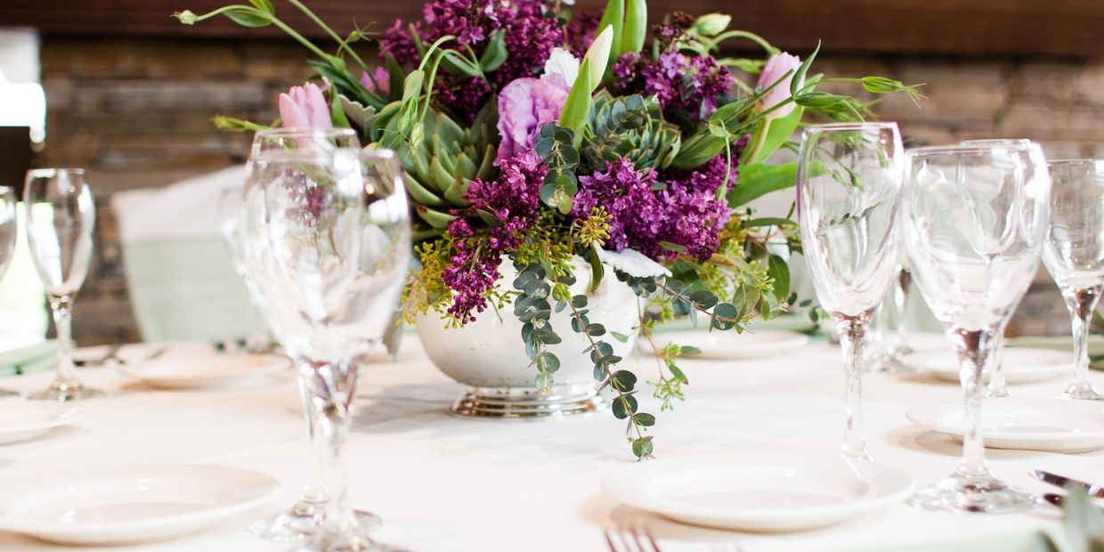 Elegant table setting with a vibrant purple floral centerpiece and clear glassware.