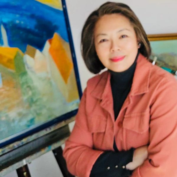 Woman in a coral jacket smiling near a colorful painting.
