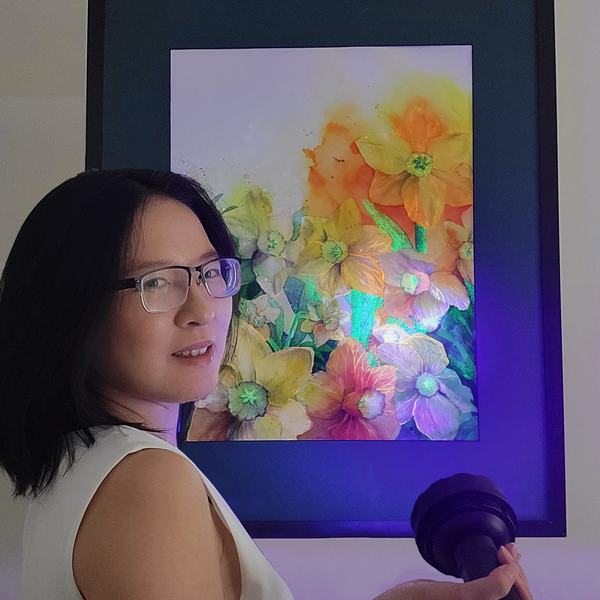 Woman holding a light in front of a colorful flower painting.