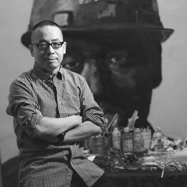Man in glasses posing in front of a large portrait painting.