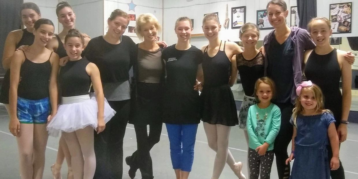Group of ballet dancers and young children posing in a dance studio.