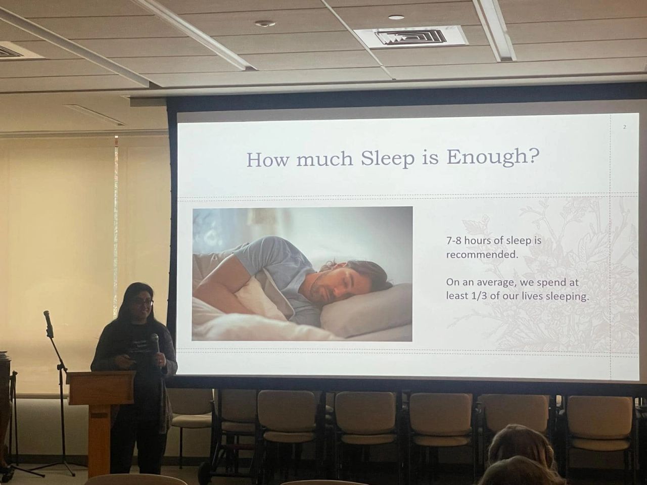 Reshma talking about "How much sleep is enough?" with slide on screen of man sleeping on side in bed with pillow.