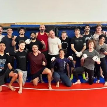 Group of martial artists posing in a training gym with gloves and hand wraps.