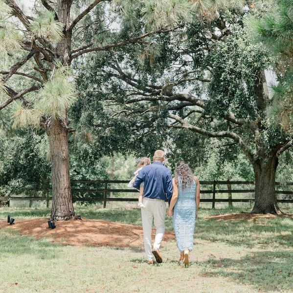 A family of three walking together in a sunny, tree-filled backyard.