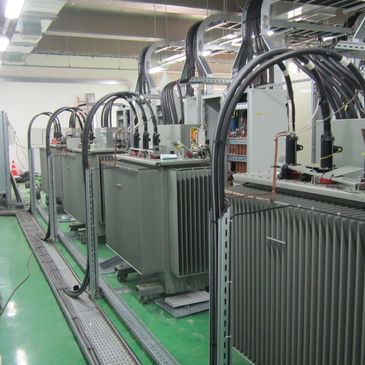 Large industrial electrical transformers connected with thick cables in a factory setting.