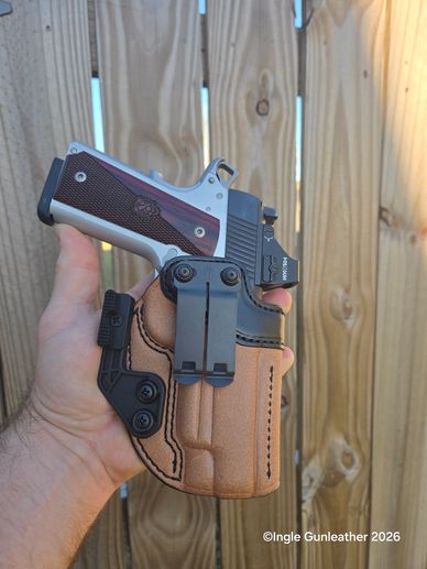 Hand holding a pistol in a leather holster against a wooden fence.