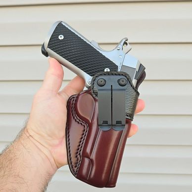 Hand holding a handgun in a brown leather holster against a beige background.