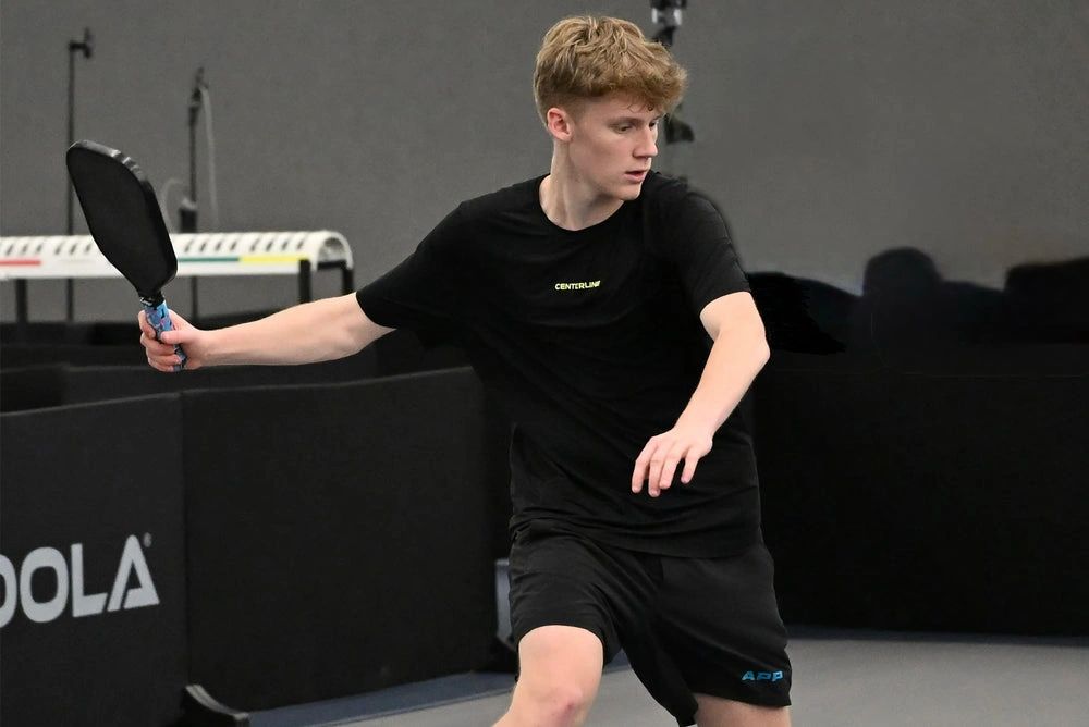 Young man playing pickleball indoors with focused expression.