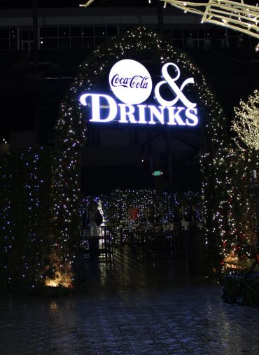 Illuminated Coca-Cola & Drinks sign at a festive entrance adorned with twinkling lights.