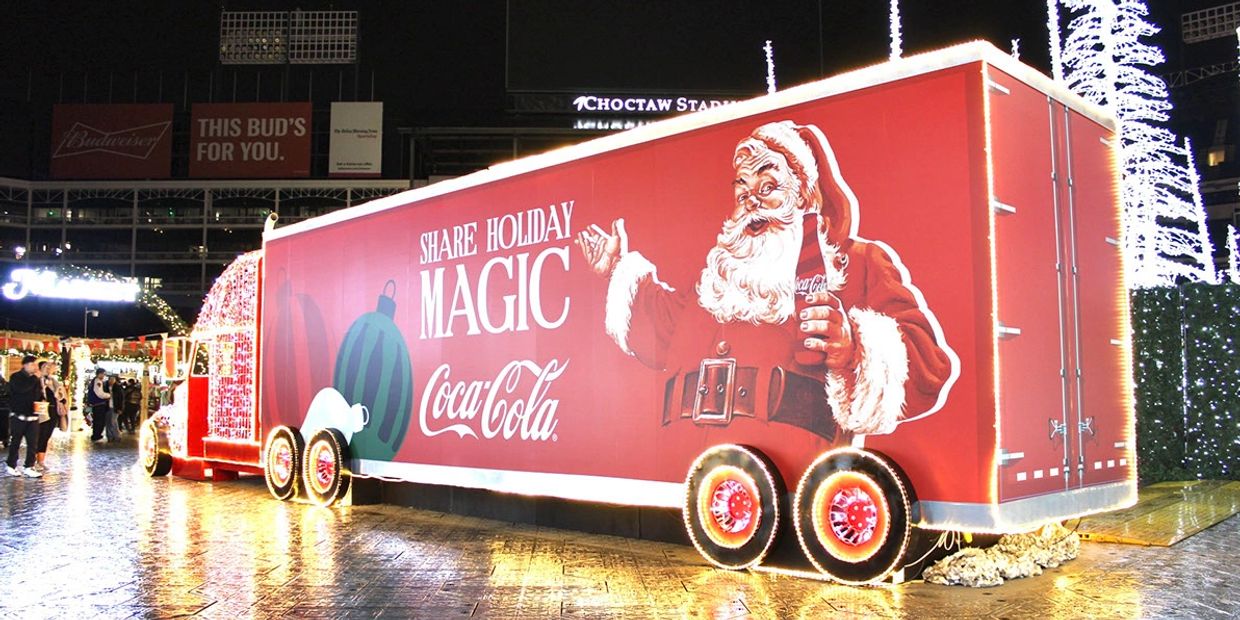A festive Coca-Cola truck decorated with Santa and holiday lights at night.