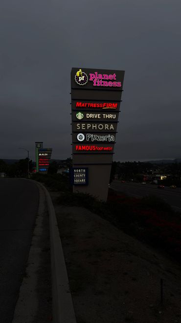Illuminated shopping center sign at dusk showcasing various stores and services.