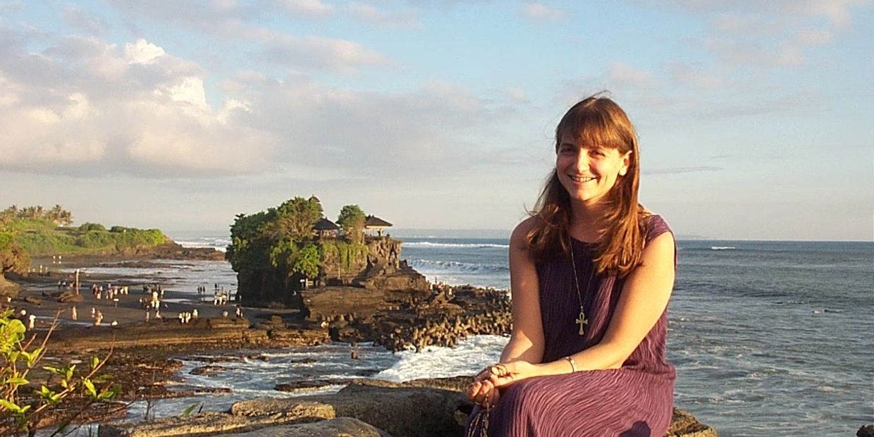 Woman smiling by the ocean on rocky shore.