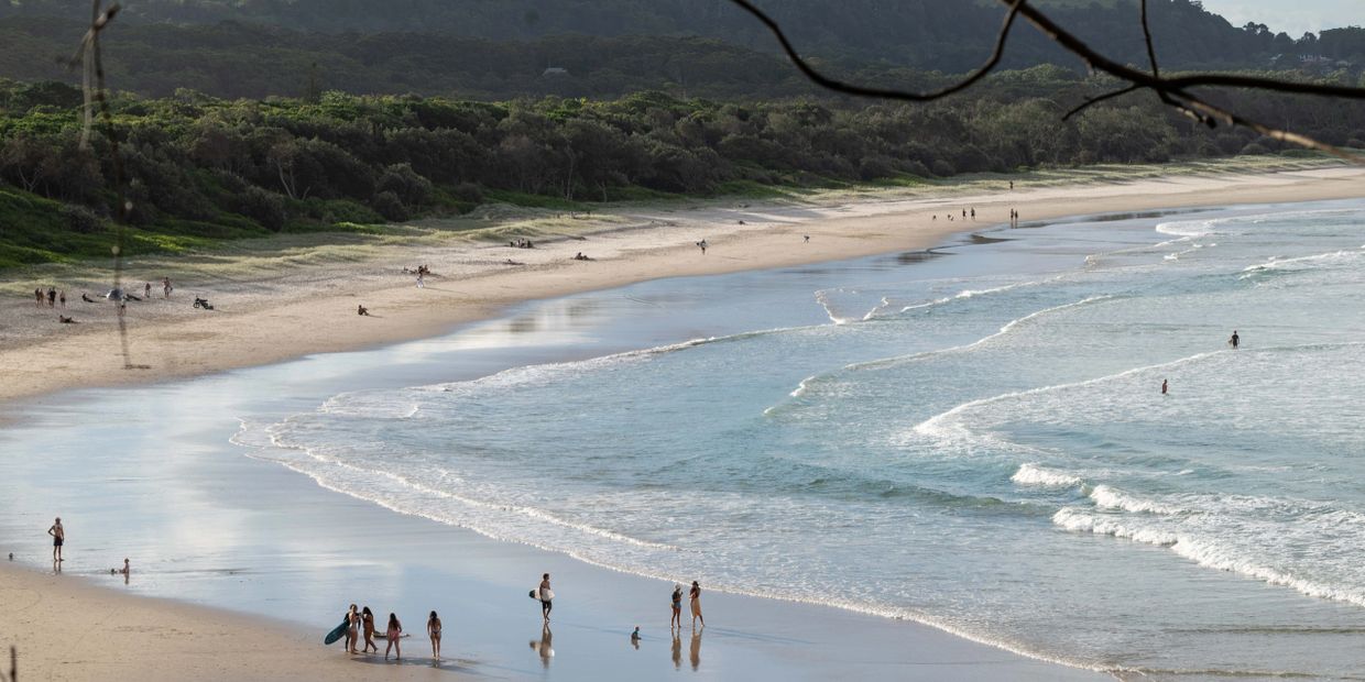People enjoying a calm beach with gentle waves and forest backdrop.