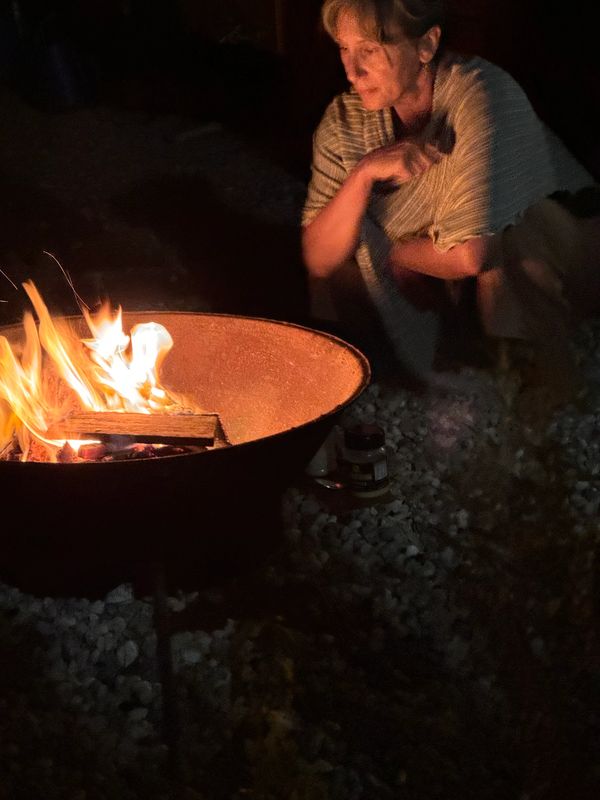 Person wrapped in blanket sitting by a fire pit at night.