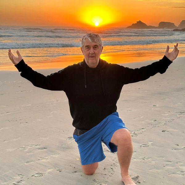 Man kneeling on beach at sunset with arms outstretched.