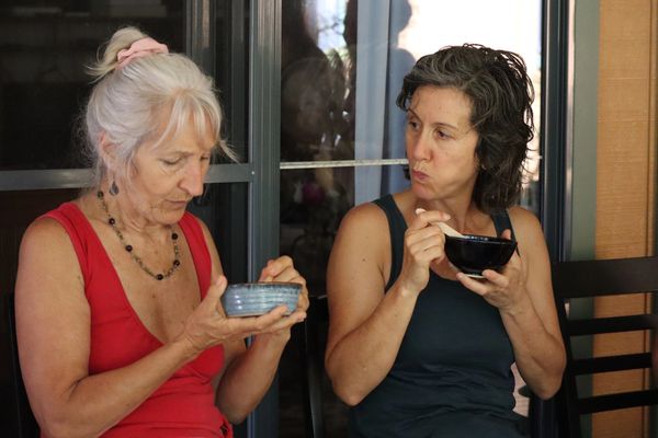 Two women eating and sitting near a window.